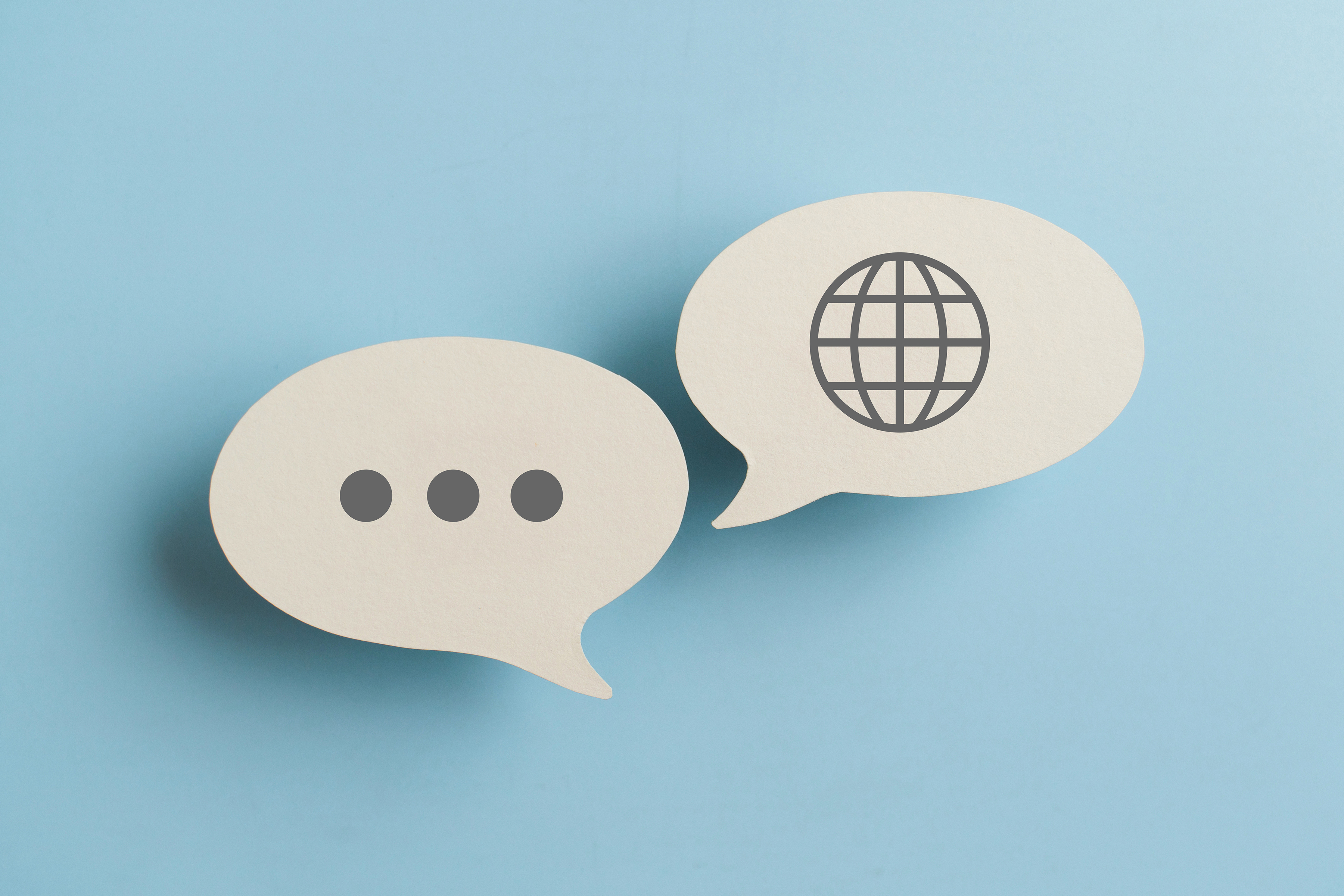 Speech bubbles, one with an ellipsis and the other with a globe, on a light blue background.