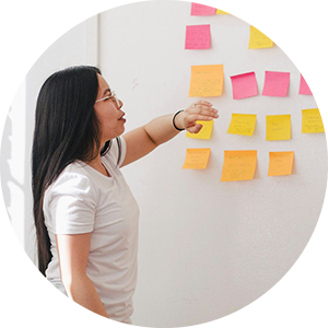 Person standing at the front of a working group talking about multi-colored sticky notes on a wall.