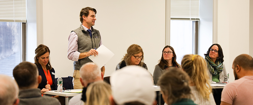 Department of Housing and Community Development Commissioner Josh Hanford participated on a panel with other public officials at a public meeting and stood to address seated attendees.